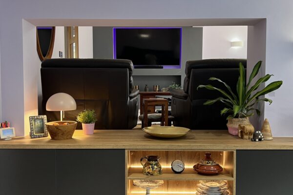 Dark grey kitchen with natural oak worktop and illuminated open shelving leading into the living area