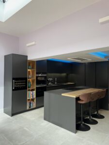 Loughton kitchen with Caneo dark graphite cabinetry, natural oak island and open illuminated shelving